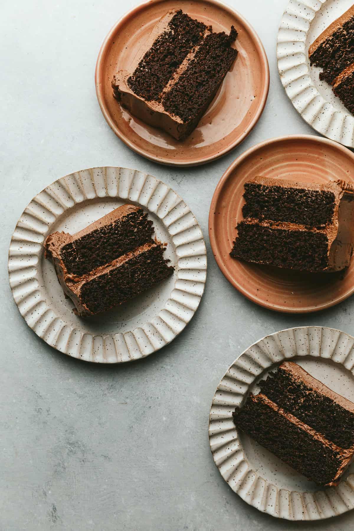 Cake plates with slices of keto chocolate cake on a gray marble surface.