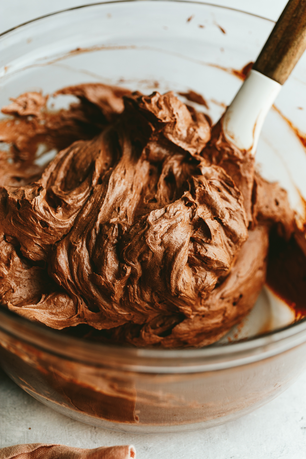 Keto chocolate frosting in a glass mixing bowl with a white spatula.