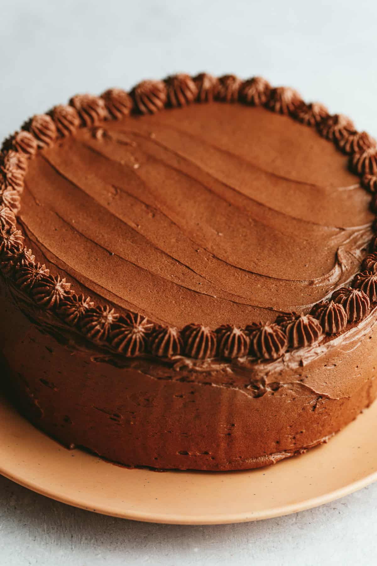 A frosted keto chocolate cake on a peach plate.