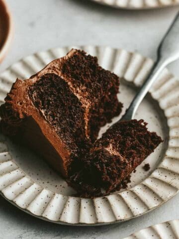 A slice of keto chocolate cake on a scalloped plate with a fork cutting a bite out of it.