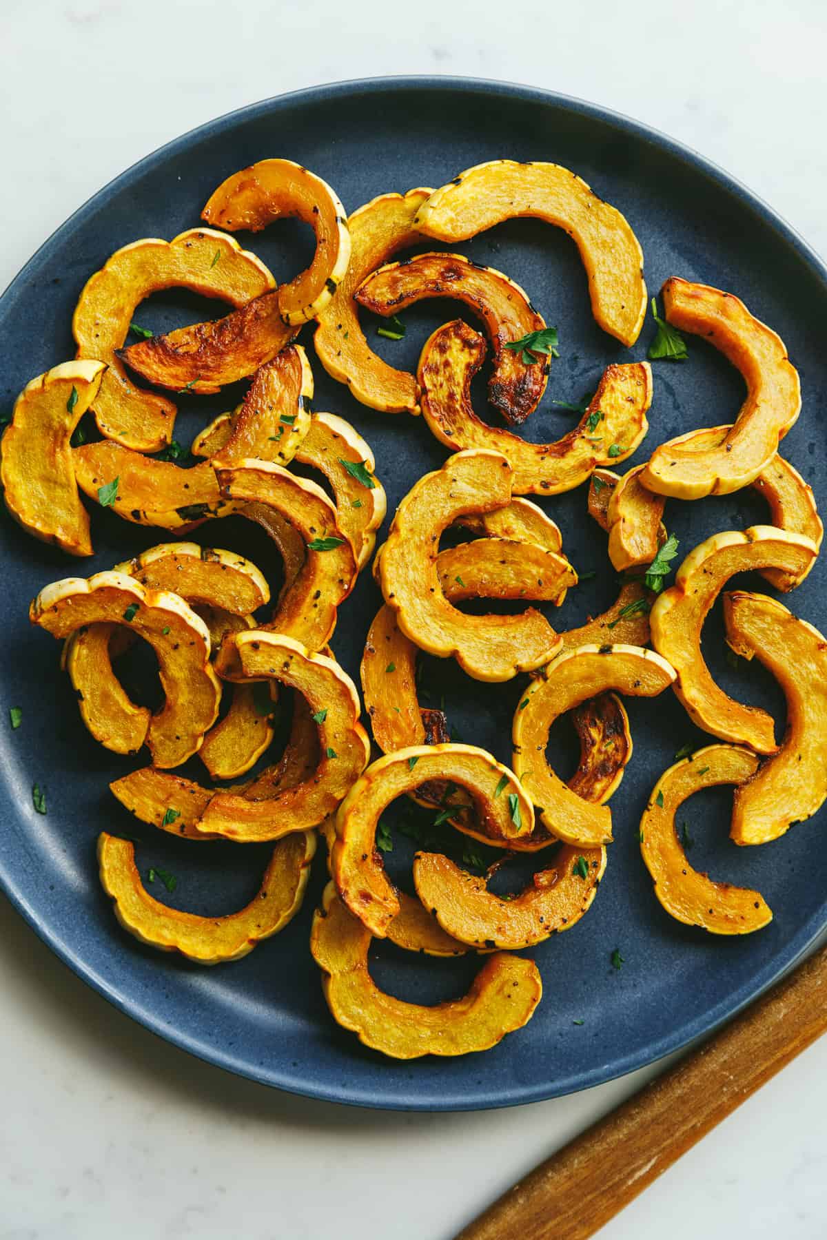 Roasted delicata squash on a blue serving plate with a wooden spoon.